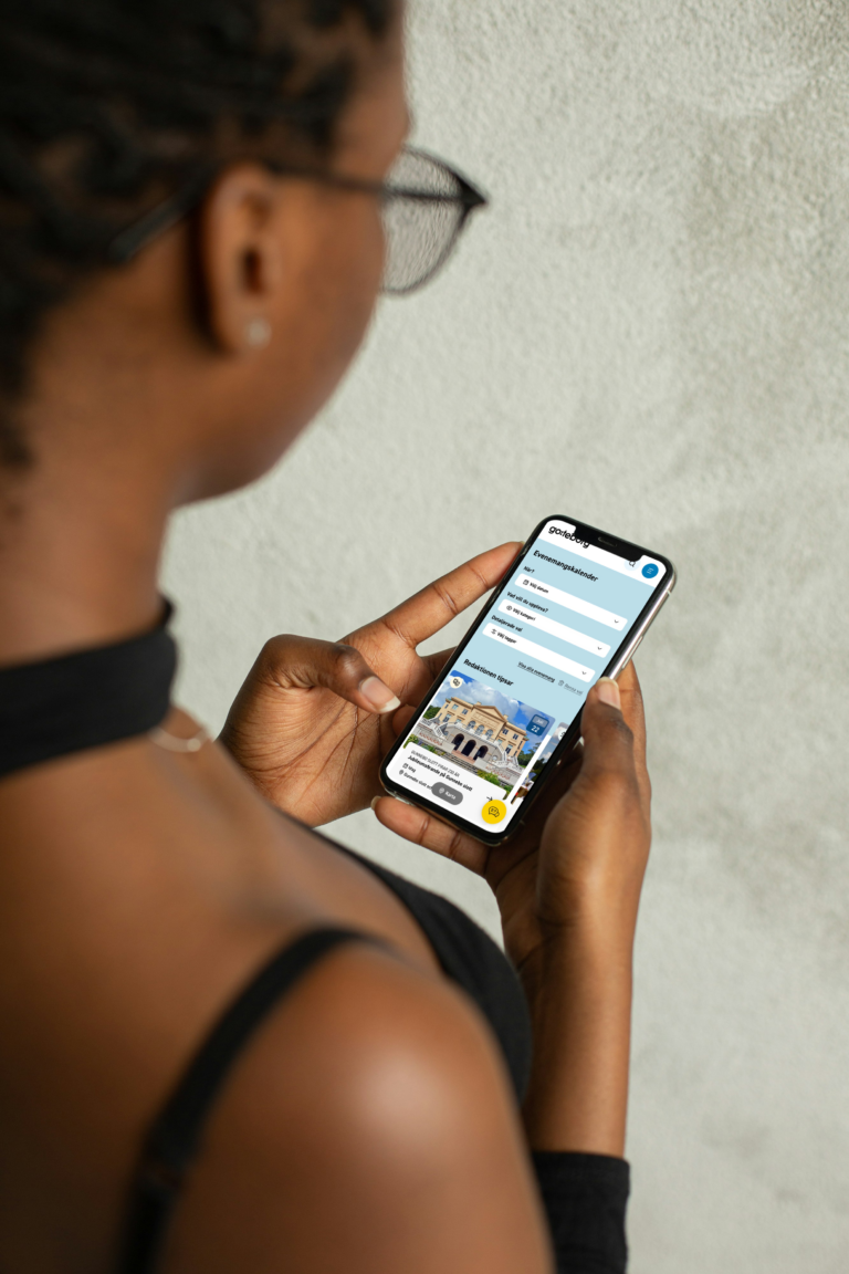 A woman is browsing the responsive website goteborg.com on a smartphone, which displays a mobile view featuring guides and cultural landmarks in Gothenburg.