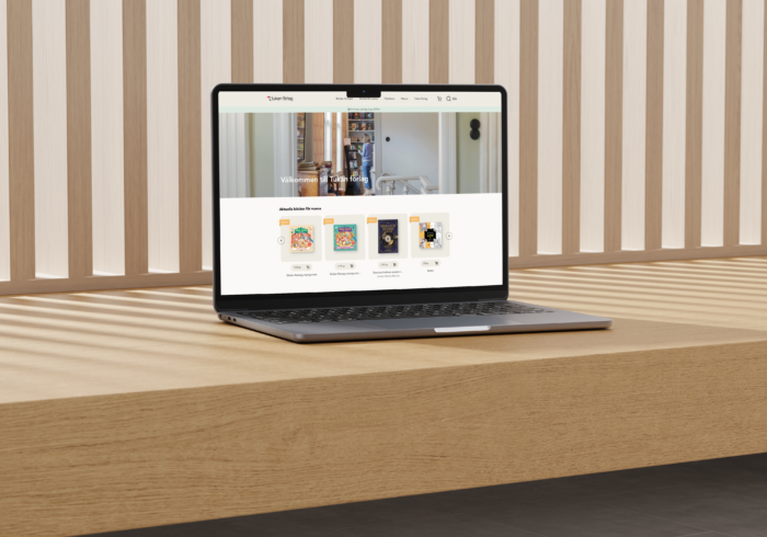 Laptop on a wooden table with the Tukan Publishing homepage displayed on the screen, in front of a patterned wooden panel background